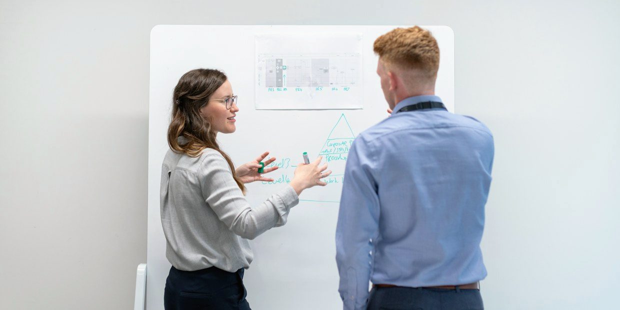 Two colleagues working through a plan at a whiteboard